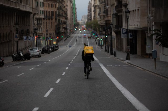 Un trabajador de Glovo en bicicleta por una calle de Barcelona, prácticamente vacía durante el primer día laborable de la segunda semana desde que se decretó el estado de alarma, en Barcelona/Catalunya (España) a 23 de marzo de 2020.