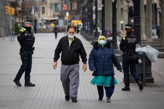 Dos agentes de la Policía y dos personas protegidas con mascarillas, durante el segundo día laborable del estado de alarma por el coronavirus, en Barcelona (España), a 17 de marzo de 2020.