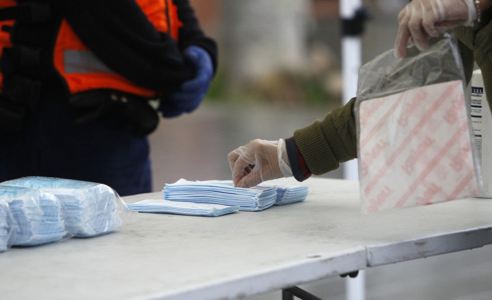 Transeúntes recogen mascarillas puestas a disposición de viajeros y usuarios de transporte público en las inmediaciones de la estación Intermodal