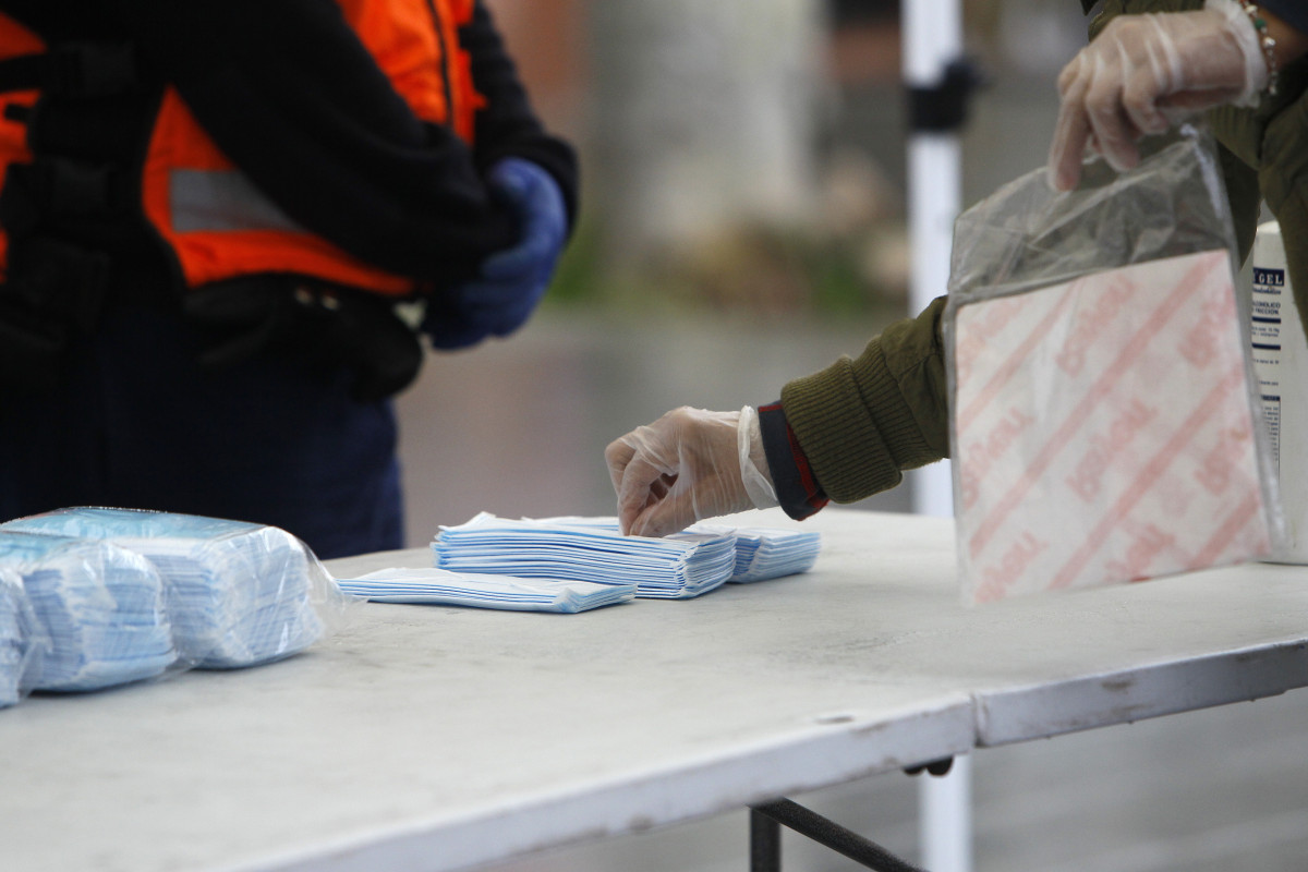 Transeúntes recogen mascarillas puestas a disposición de viajeros y usuarios de transporte público en las inmediaciones de la estación Intermodal