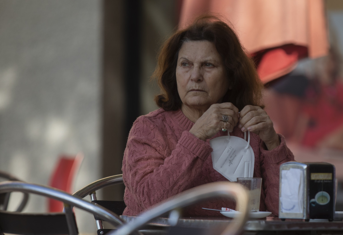 Una mujer en la terraza de un bar con la mascarilla en la mano, mientras continúa el cierre perimetral en Montequinto (Dos Hermanas), al entrar en nivel 4 de alerta  desde el pasado 20 de enero cuando superó la tasa de incidencia de Covid-19 de 500 casos
