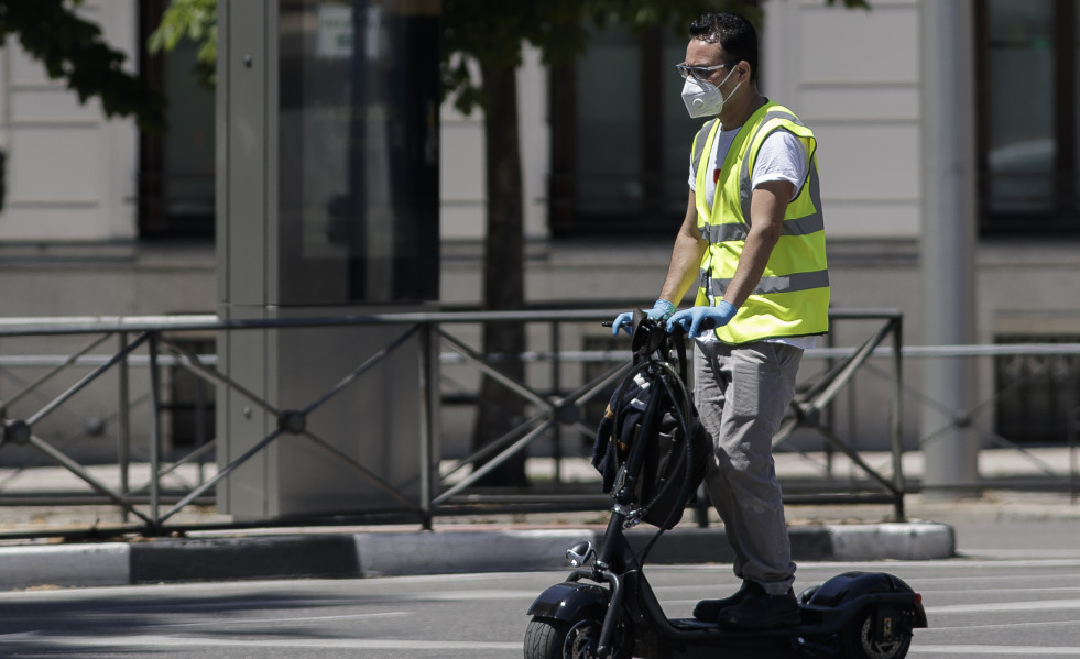 Un hombre protegido con mascarilla monta en un patinete eléctrico