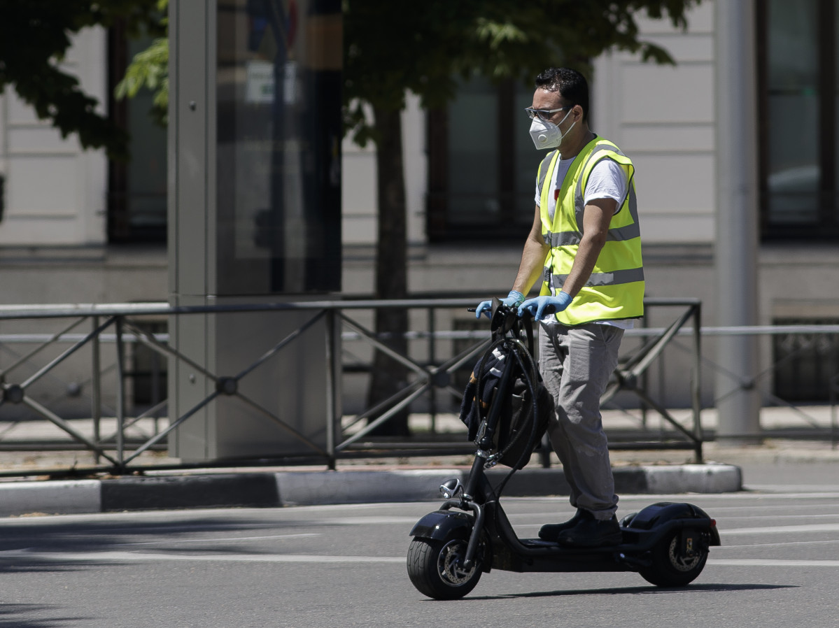 Un hombre protegido con mascarilla monta en un patinete eléctrico