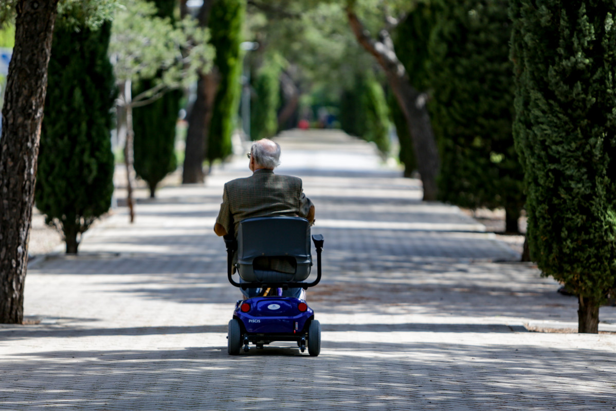 Archivo - Un anciano en silla de ruedas eléctrica en un parque en Madrid.