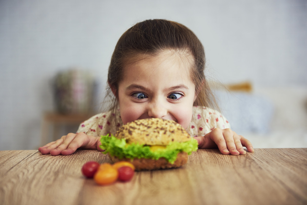 Chica juguetona mirando deliciosa hamburguesa