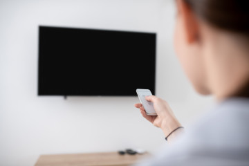 Mujer encendiendo el televisor de plasma montado en la pared
