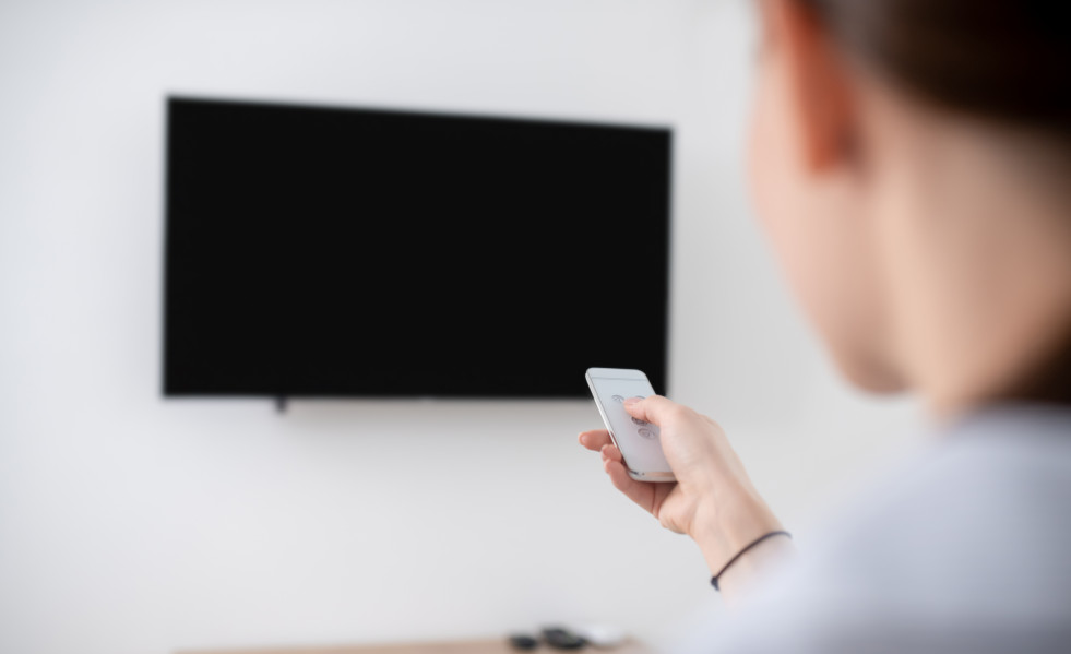 Mujer encendiendo el televisor de plasma montado en la pared