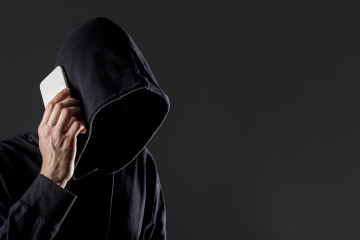 Vista lateral del pirata informatico masculino hablando por telefono inteligente con espacio de copia