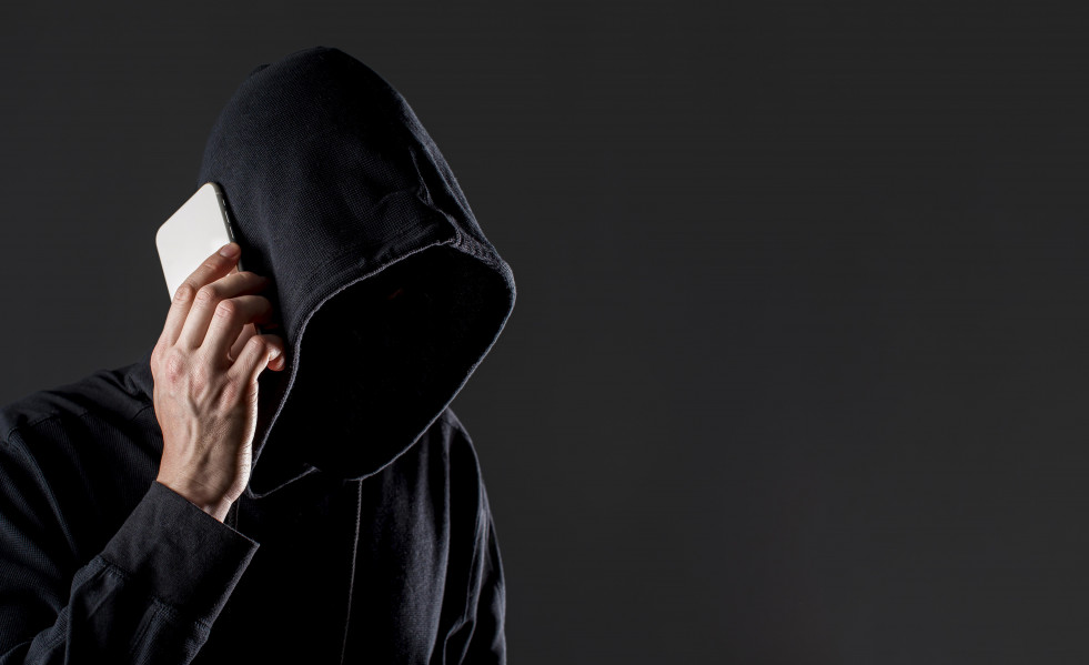 Vista lateral del pirata informatico masculino hablando por telefono inteligente con espacio de copia