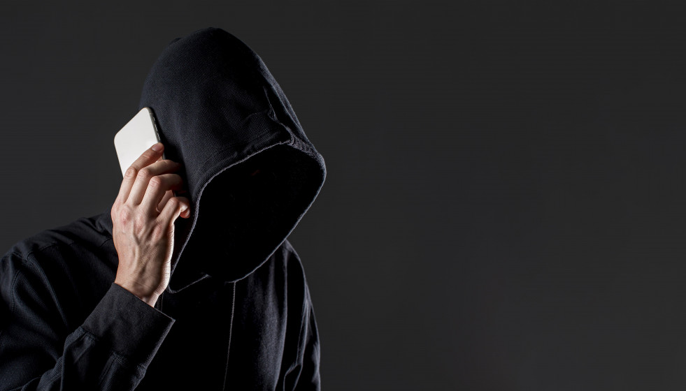 Vista lateral del pirata informatico masculino hablando por telefono inteligente con espacio de copia