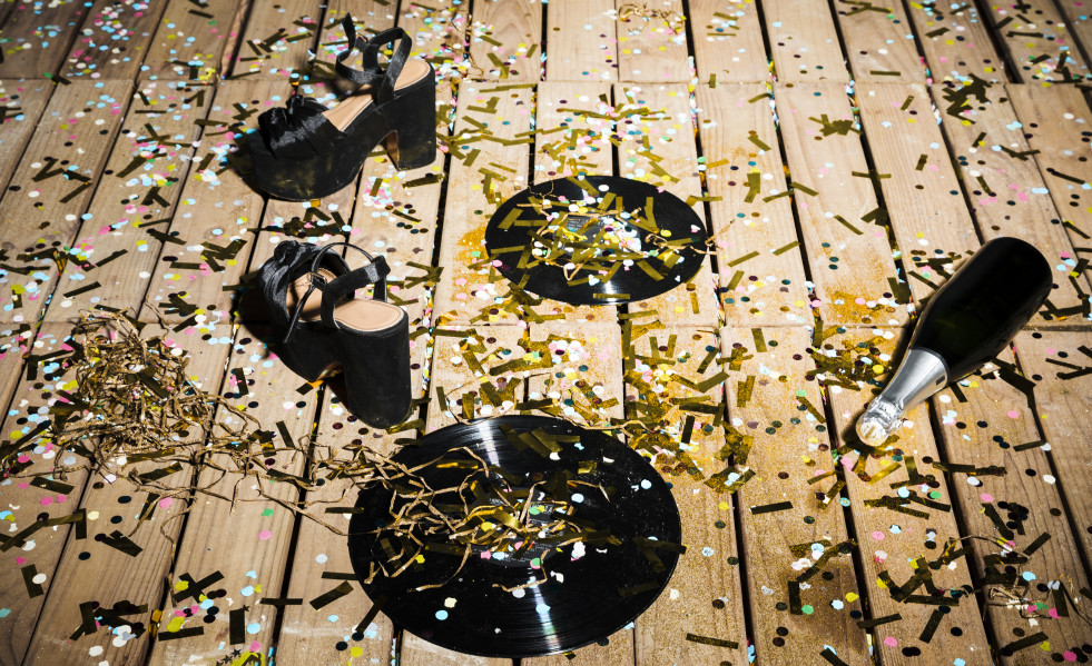 Discos de vinilo zapatos de mujer y botella de bebida entre confeti