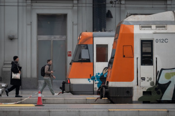 Archivo - Dos personas frente a dos trenes de Rodalies.