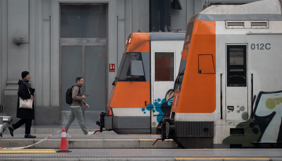 Archivo - Dos personas frente a dos trenes de Rodalies.