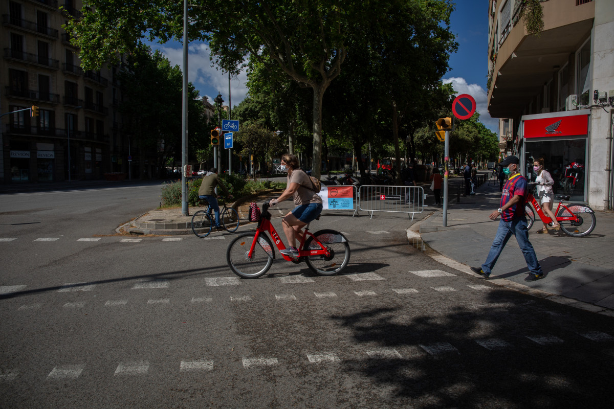 Transeúentes pasan al lado de las vallas instaladas para cortar el tráfico lateral de la Diagonal. En Barcelona, Catalunya (España), a 13 de mayo de 2020.