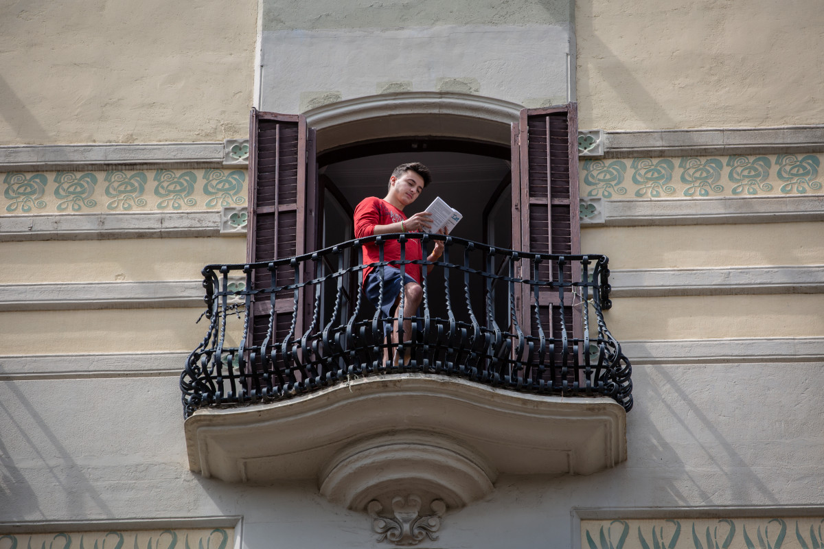 Un joven lee un libro en el balcón de su casa con ocasión de la Diada de Sant Jordi, en la que es costumbre regalar libros y rosas, en Barcelona / Catalunya (España), a 23 de abril de 2020.