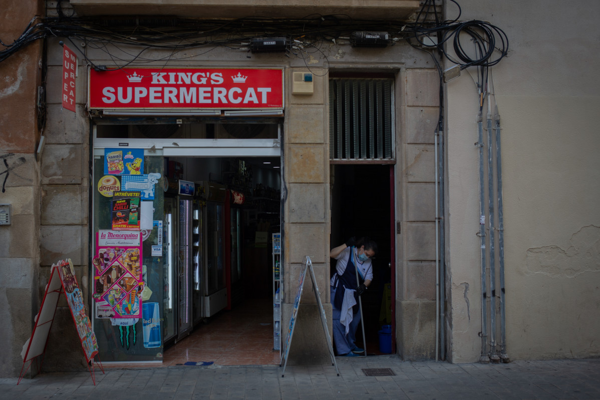 Una mujer friega un portal junto a un supermercado abierto durante el tercer día de la entrada en vigor de las nuevas restricciones en Cataluña, en Barcelona, Cataluña (España) a 19 de octubre de 2020. El pasado viernes 16 de octubre entraron en vigor las