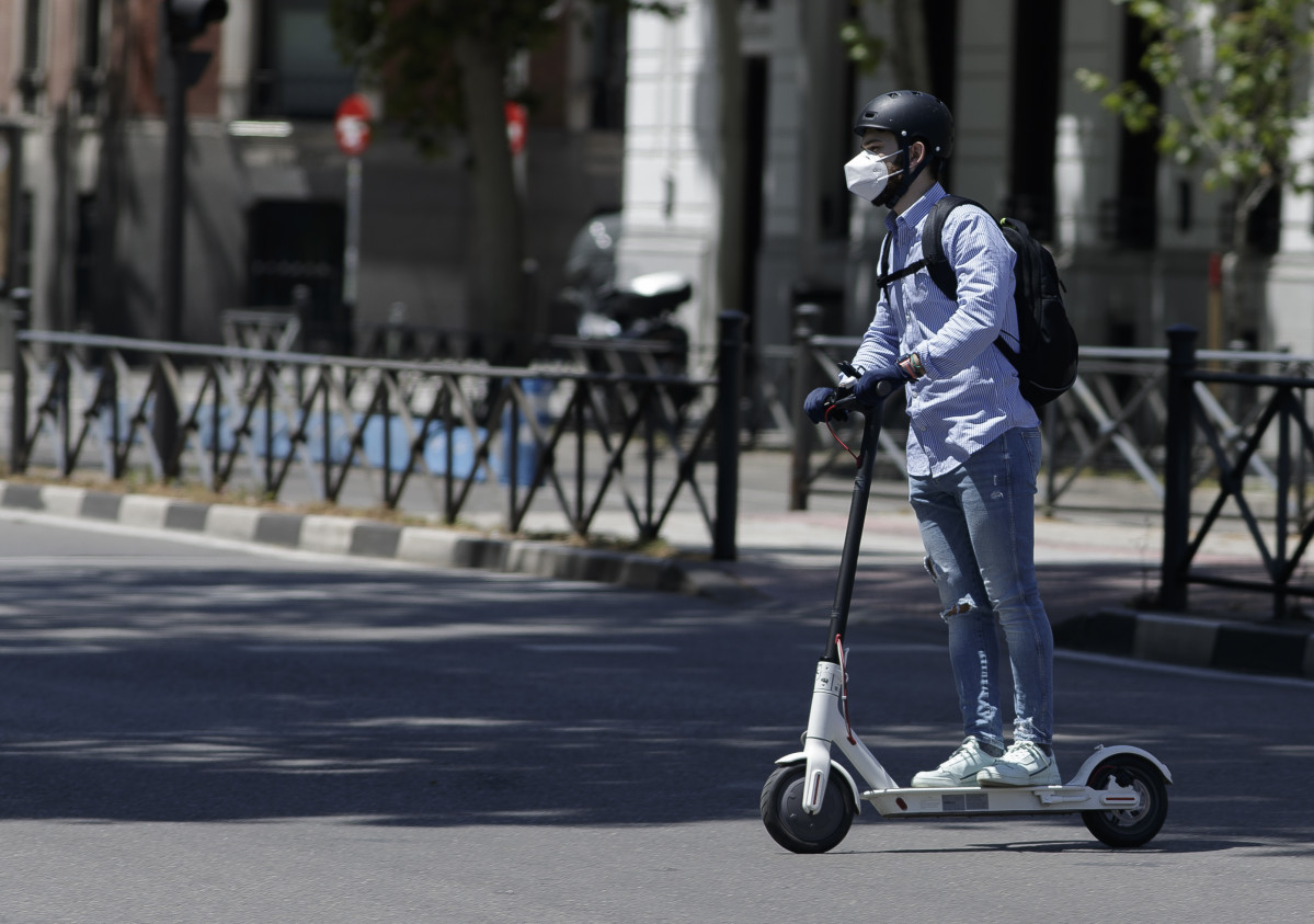 Un hombre protegido con mascarilla monta en un patinete eléctrico.